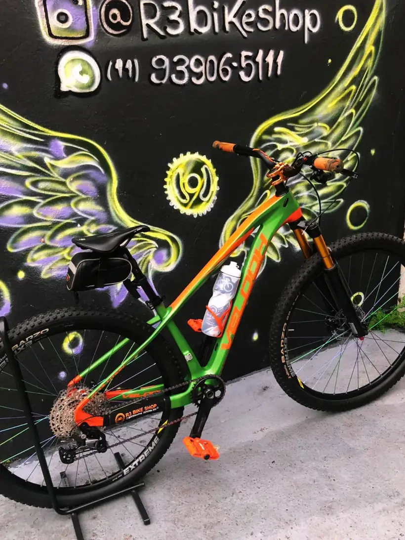 Bicicleta laranja e verde diante do mural de asas da R3 Bike Shop